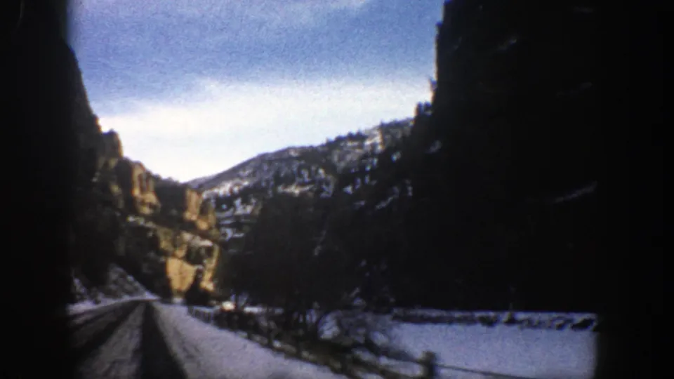 End frame of the 1961 Aspen-area drive, with snow, bare trees, roadside posts, and shadowed cliffs along the road.