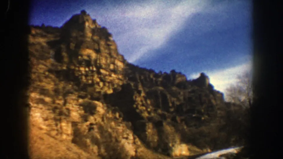 1961 Aspen-area travel frame with rugged cliff walls, a bend in the road, snow along the valley floor, and winter sky overhead.