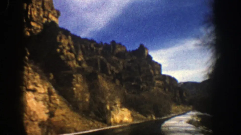 Aspen, Colorado road scene from 1961 8mm footage, with sunlit rock walls and snow beside the pavement.