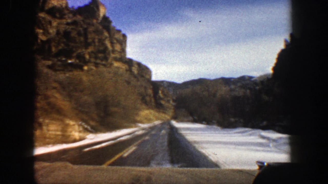 Car-window view of a snowy divided mountain highway beside rocky cliffs.