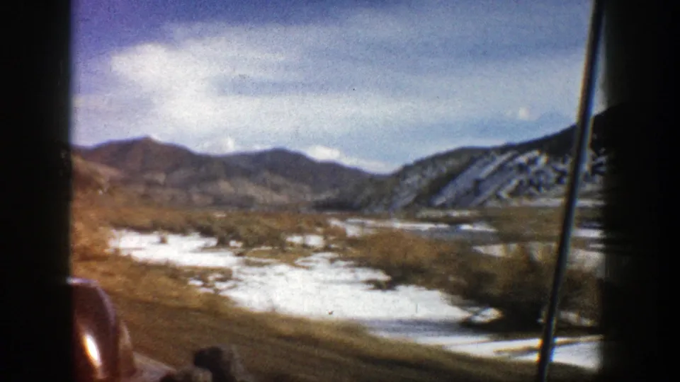 Aspen-area mountain landscape in 1961, viewed from inside a moving car with snow, brush, water, and hills visible.