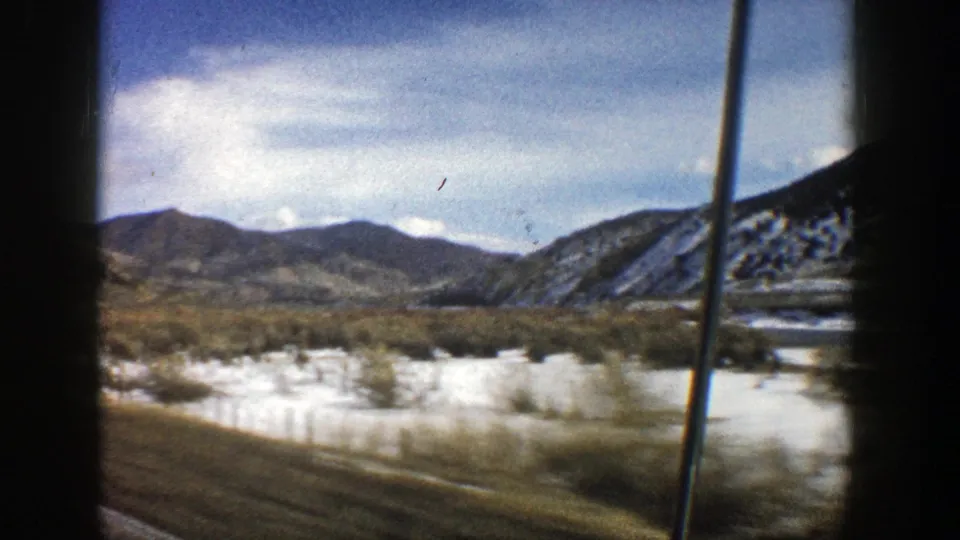 Aspen, Colorado home-movie frame showing snow-covered brushland, hills, and sky from a moving car in 1961.