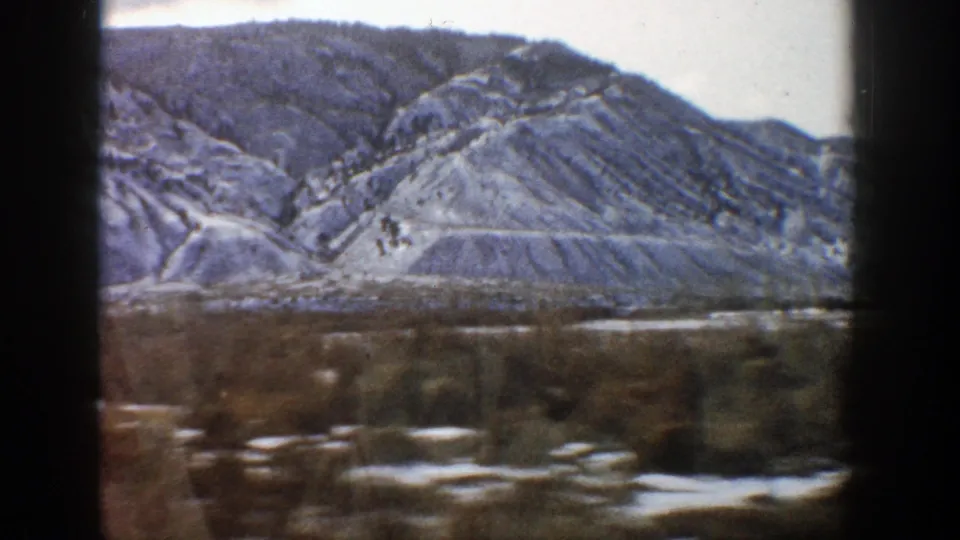 Aspen, Colorado home-movie frame from 1961 with layered rocky slopes, scattered snow, and a soft, motion-blurred foreground.