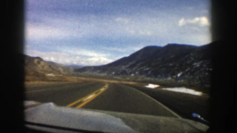 Vintage 8mm road-trip frame from Aspen, Colorado, showing the car hood and mountain road ahead.