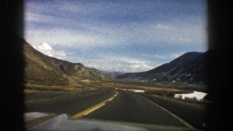 Inside-car 8mm view of a winding road near Aspen, Colorado, with rugged hills and a distant valley under clouds.