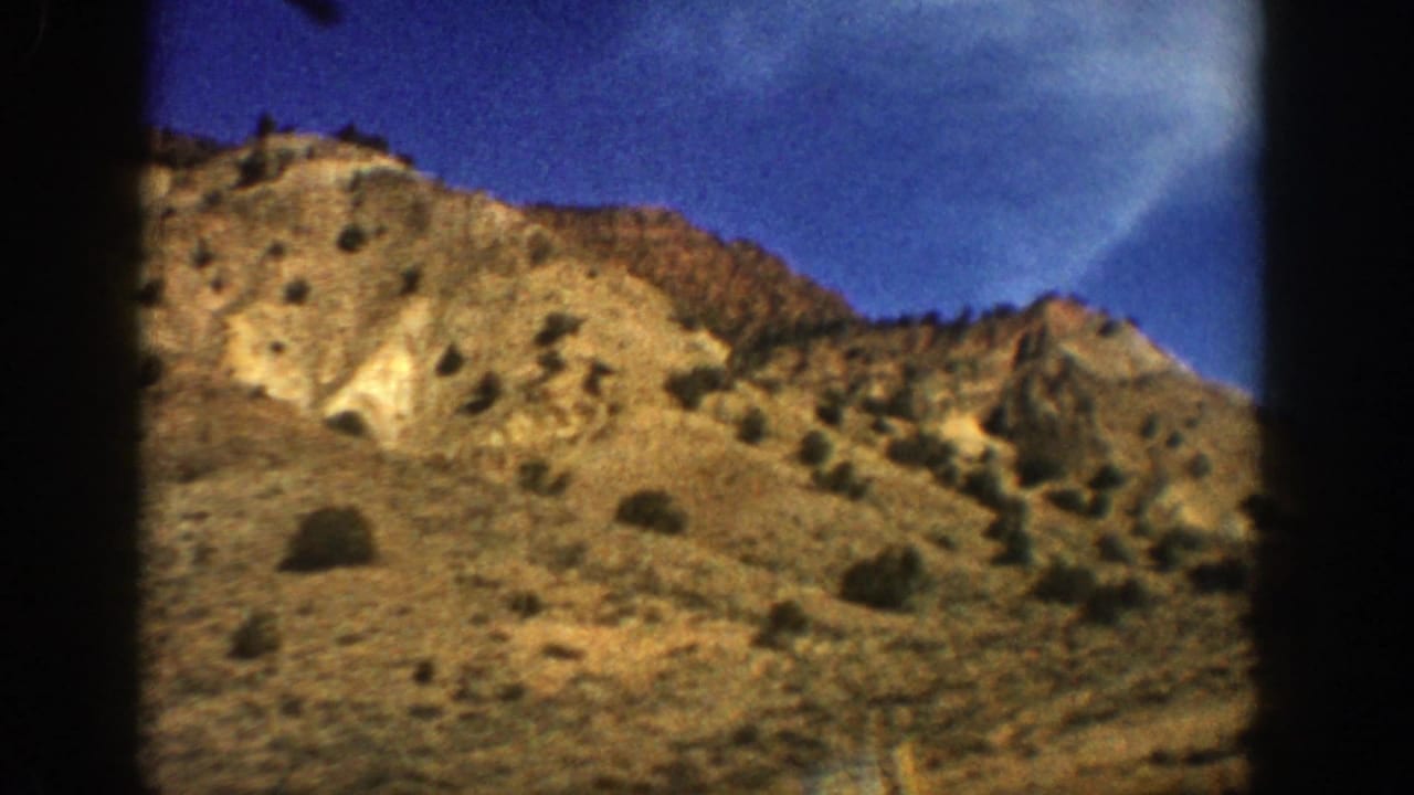 1961 Aspen, Colorado 8mm frame showing tan arid mountain terrain, sparse shrubs, dry grass, and deep blue sky.