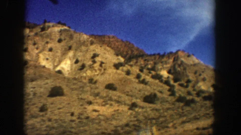1961 Aspen, Colorado 8mm frame showing tan arid mountain terrain, sparse shrubs, dry grass, and deep blue sky.