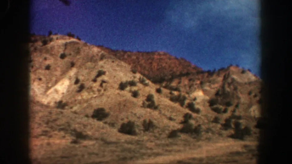 Vintage 8mm view of Aspen, Colorado terrain with eroded tan slopes, sparse vegetation, and saturated blue sky.