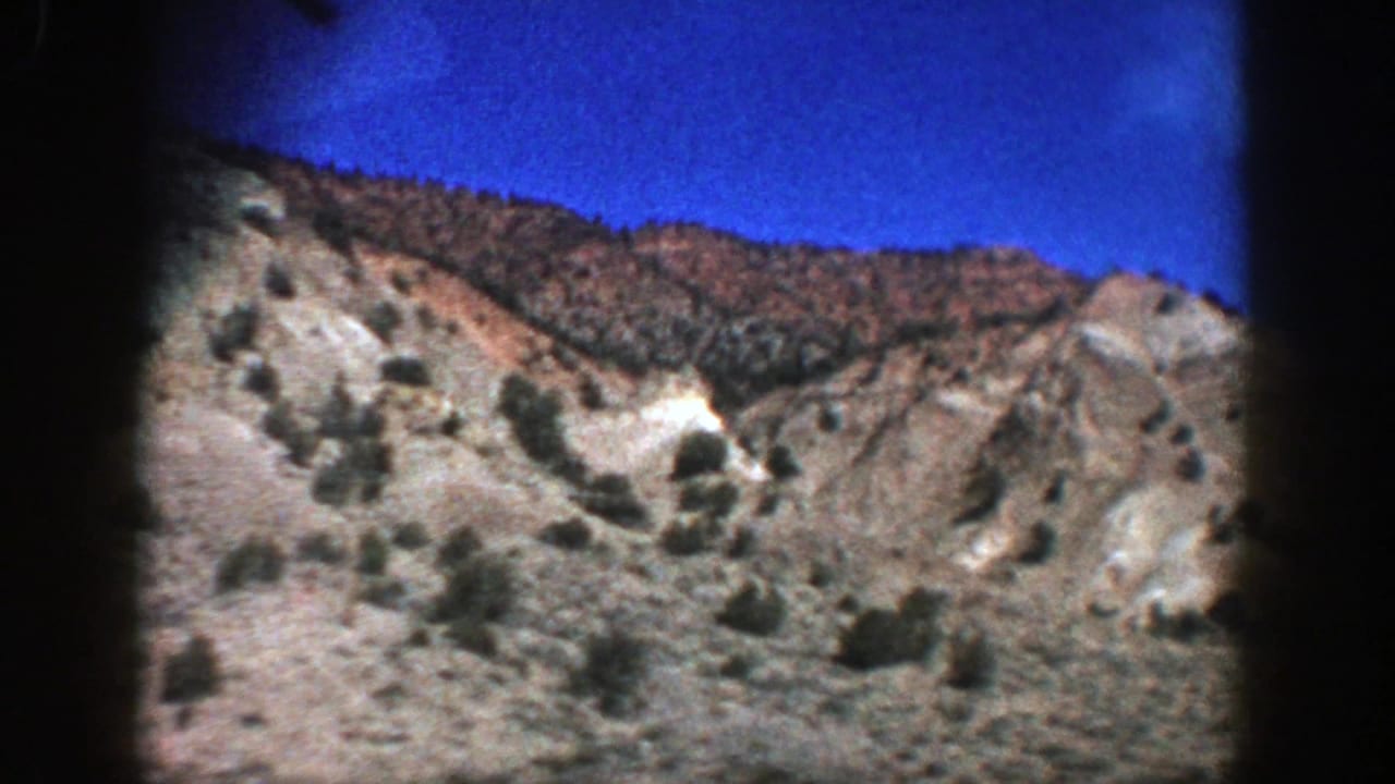 Dry rocky hillside with sparse shrubs under a deep blue sky.