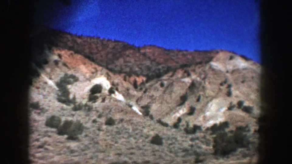 Home-movie view near Aspen, Colorado, with pale eroded slopes, scrub plants, and saturated blue sky framed by 8mm edges.