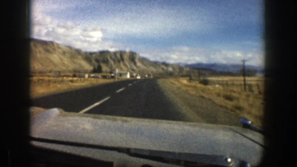 1961 home-movie view from inside a vehicle approaching tan Colorado hills along a paved road.