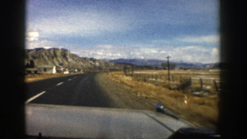 Passenger-view 8mm frame from 1961 Colorado showing highway travel near tan hills and sparse roadside structures.