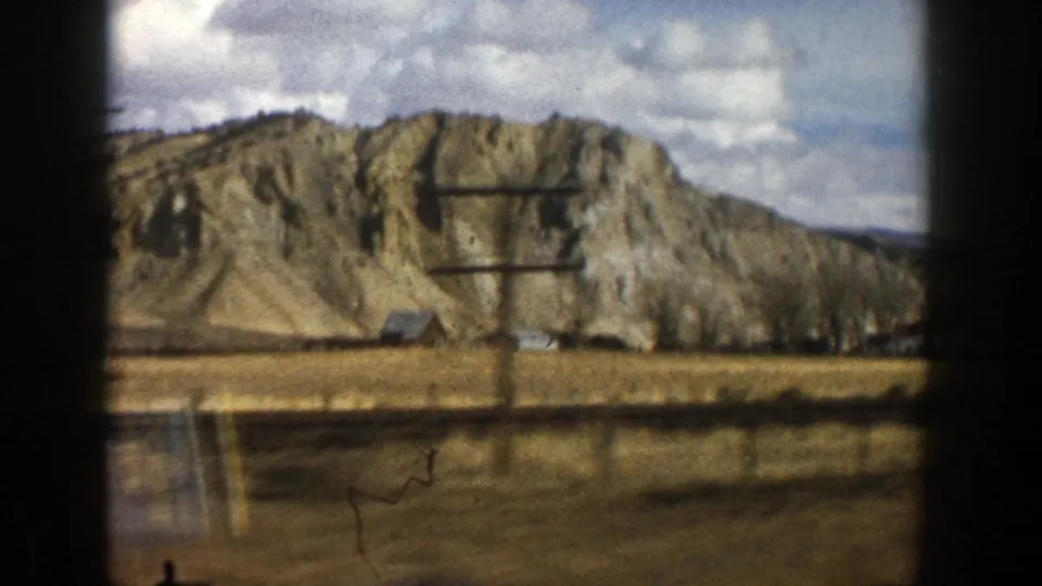 1961 Colorado home-movie frame showing a side view of a tan ridge beyond dry roadside land.