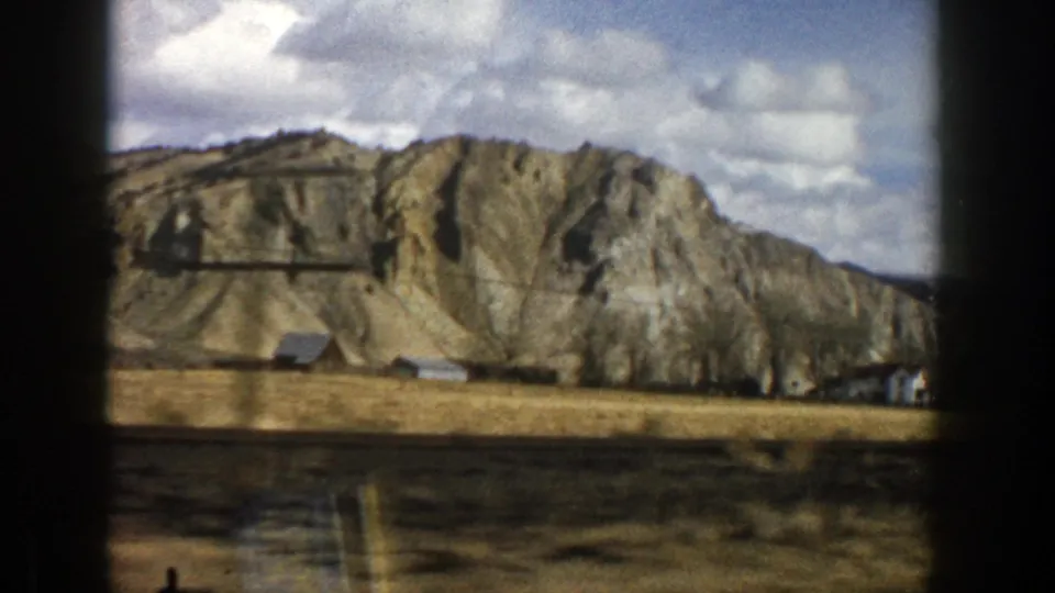 Scenic 8mm frame from Aspen, Colorado showing a layered mountain face, small structures, and open land below.