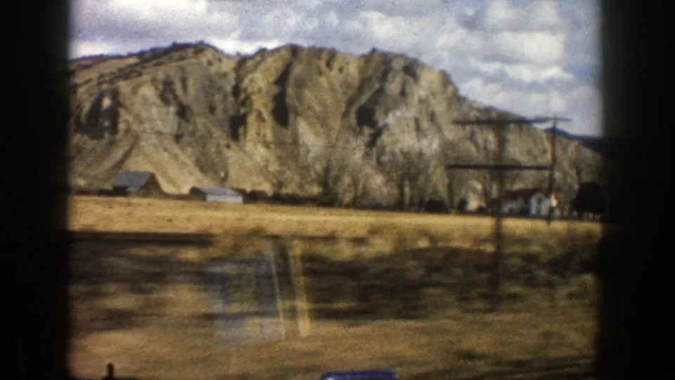 Moving 8mm travel frame showing Aspen-area mountain terrain with dry foreground land and small buildings near the foothill.