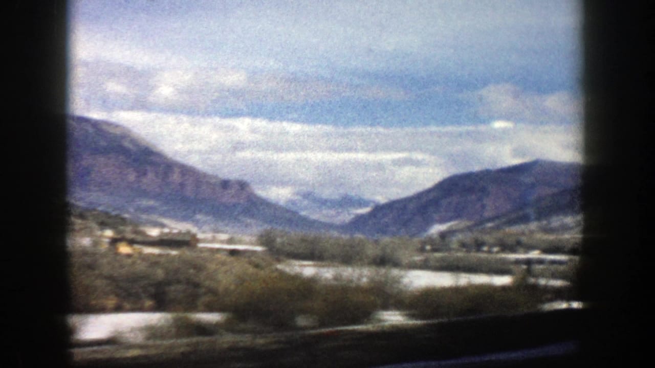 Snow-dusted valley and mountains seen through dark vehicle-window framing.