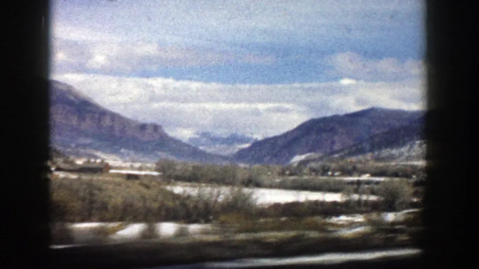 A moving 8mm view across the Aspen, Colorado valley, with snow on the ground and mountains under a cloudy sky.