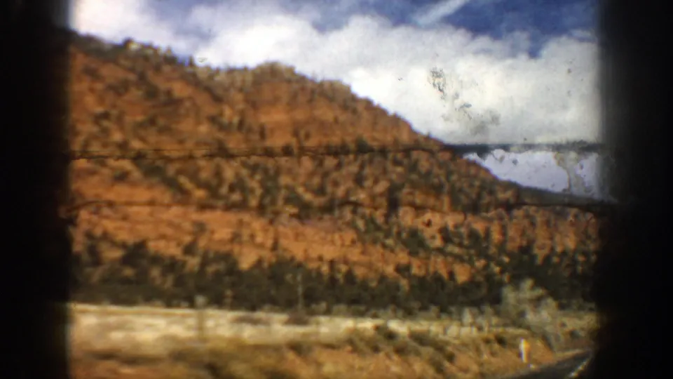 1961 8mm travel footage shows a brown Colorado hillside with sparse vegetation and roadside blur from a moving vehicle.