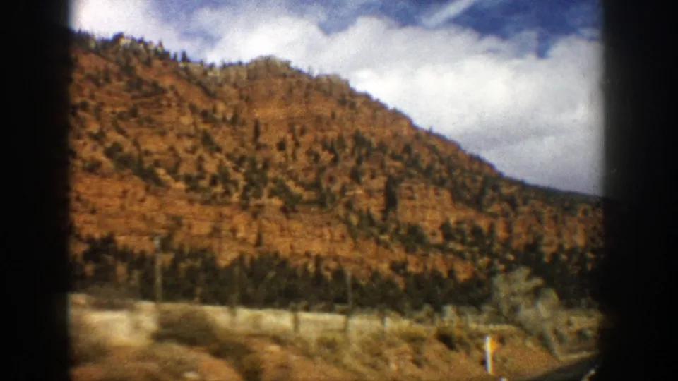 A passenger-window shot in the Aspen, Colorado area shows a brown hillside, sparse trees, and a partly cloudy sky.