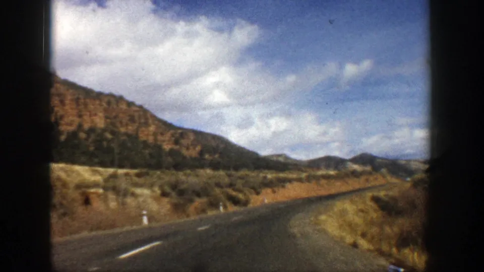 Forward-facing 8mm travel view of an empty Aspen, Colorado mountain road curving through dry hills in 1961.