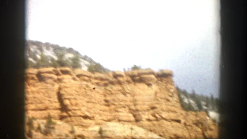 1961 Colorado 8mm frame showing a tan roadside cliff and mountain terrain, softened by motion and bright exposure.