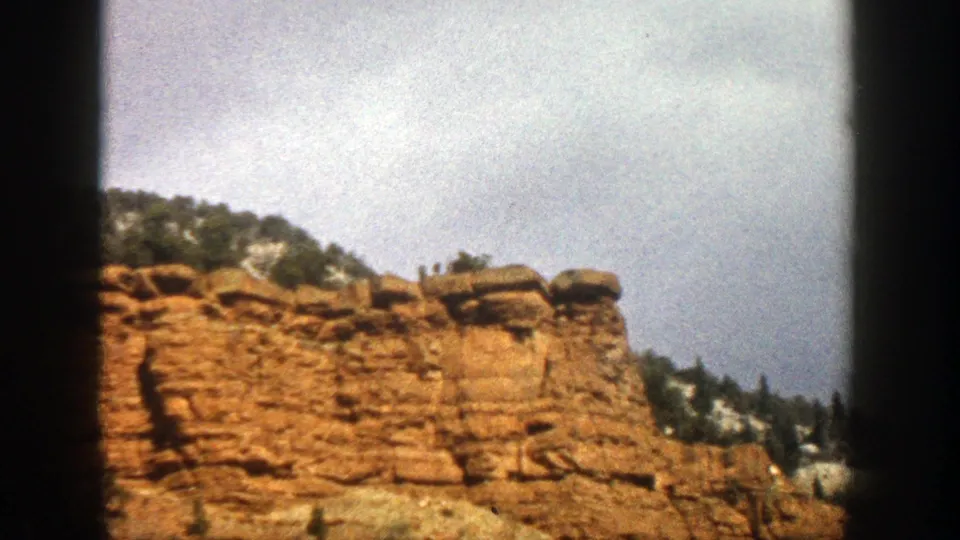 1961 Aspen-area roadside view of an orange-tan rock formation with scrub brush, mountain terrain, and pale sky in an 8mm frame.