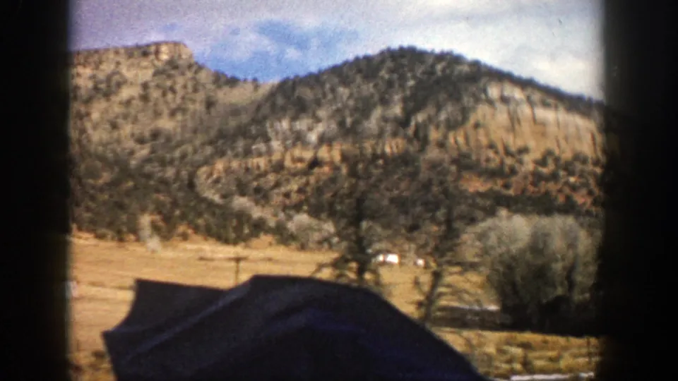 1961 Aspen, Colorado road footage showing a sandy mountain face, dry open ground, trees, and a dark vehicle-window foreground.