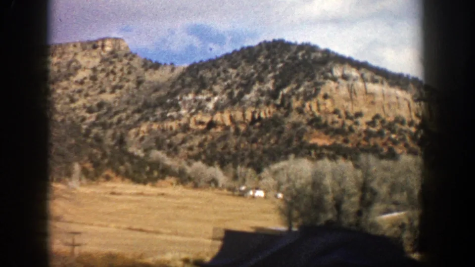 1961 Aspen, Colorado passenger view of a dry valley below a rugged ridge, framed by dark vehicle-window borders.