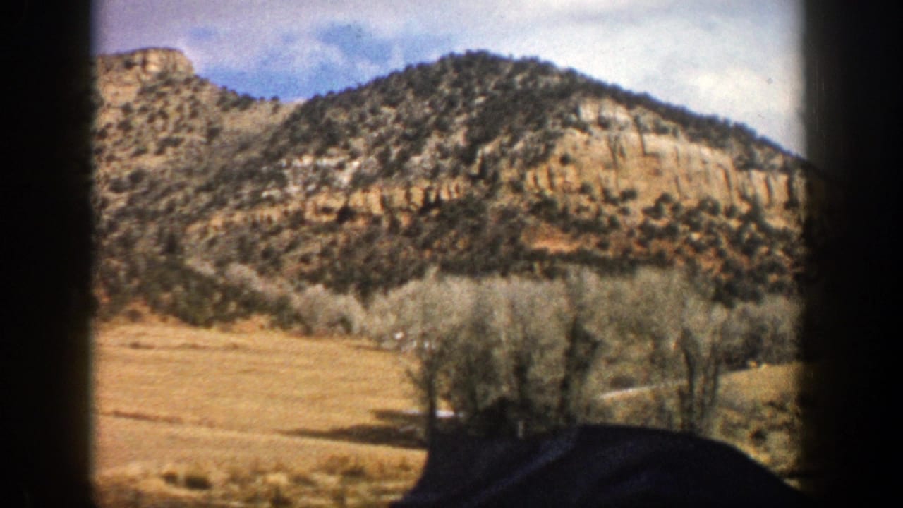 1961 Aspen, Colorado home-movie frame showing a tan cliff and wooded hillside viewed from a moving vehicle.