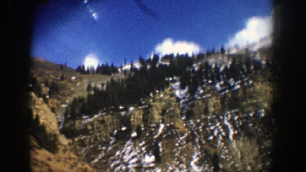 1961 Aspen-area 8mm view of a snow-patched mountain slope, evergreen trees, and blue sky with clouds.