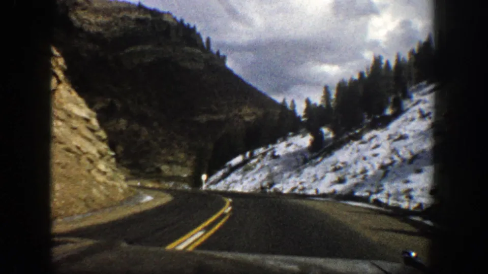 Vintage 8mm frame of a two-lane road curving between rocky and snowy slopes near Aspen, Colorado.