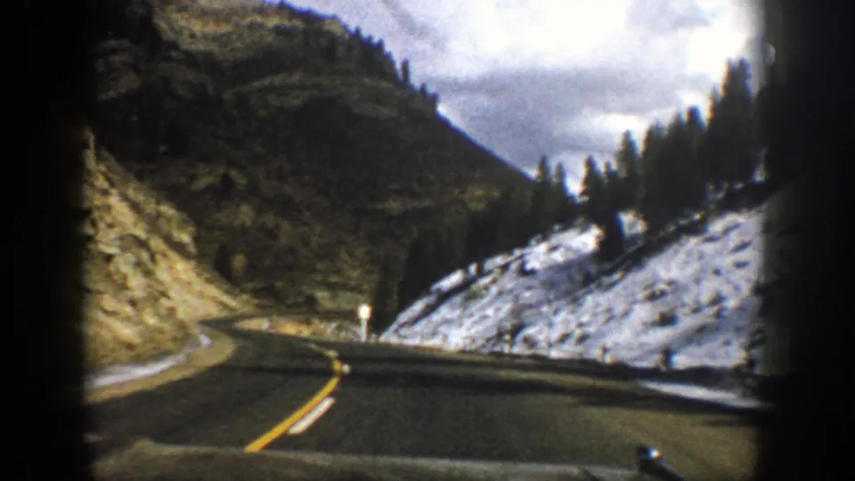 1961 8mm travel footage shows a snowy mountain roadway curving through Aspen-area terrain under a cloudy sky.