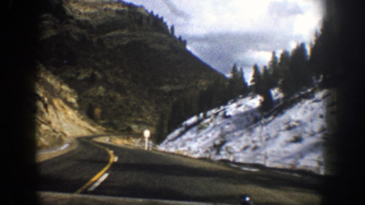 Curving mountain road with snow on the right slope and evergreen trees ahead.