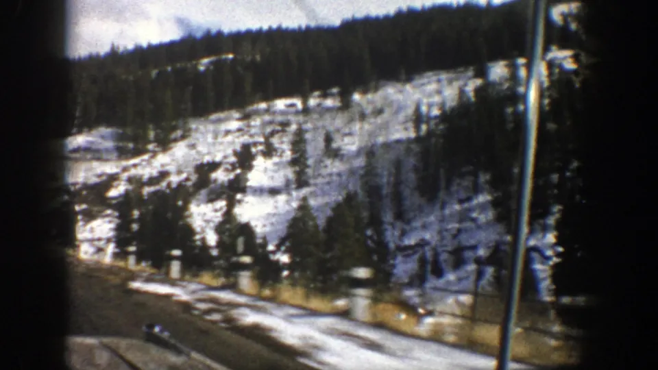 1961 Aspen, Colorado road view with patchy snow on a forested slope and dark 8mm frame edges.