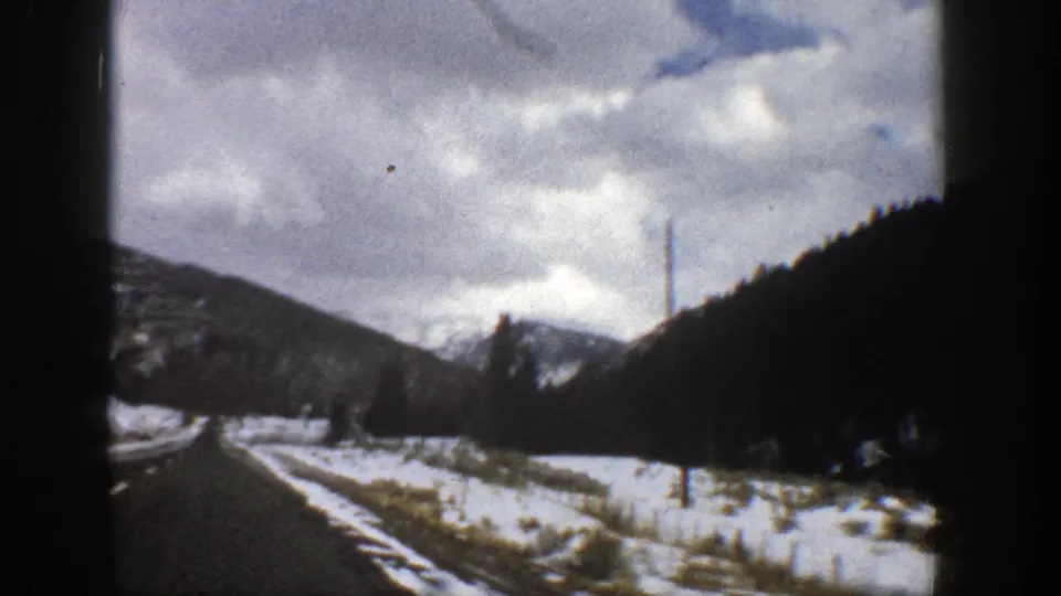 1961 Aspen-area mountain drive showing a snow-edged road, dark hillsides, distant peaks, and overcast winter sky.