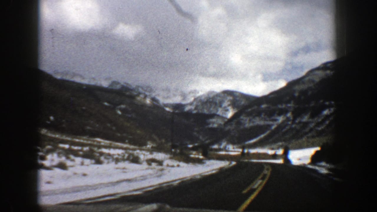 Winding mountain road with snow-covered shoulders and dark hills ahead.