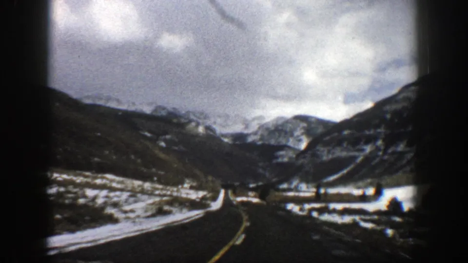 1961 Aspen, Colorado winter driving view with the road curving through a snowy mountain valley under overcast light.