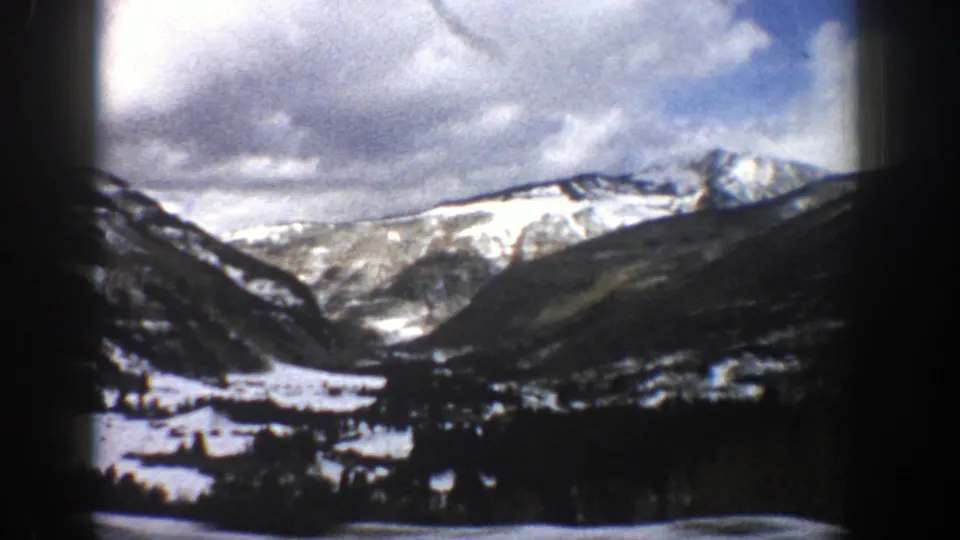 Aspen, Colorado 1961 8mm frame with a snowy valley floor, dark hillsides, and bright mountain ridge beneath a clouded sky.