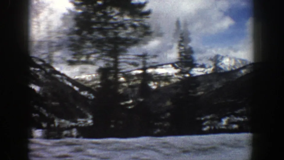 1961 Aspen, Colorado travel footage with a tall evergreen blurred by motion against snowy mountain ridges.