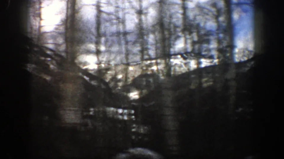 1961 Aspen, Colorado 8mm frame looking through roadside trees toward snow patches and mountain slopes.