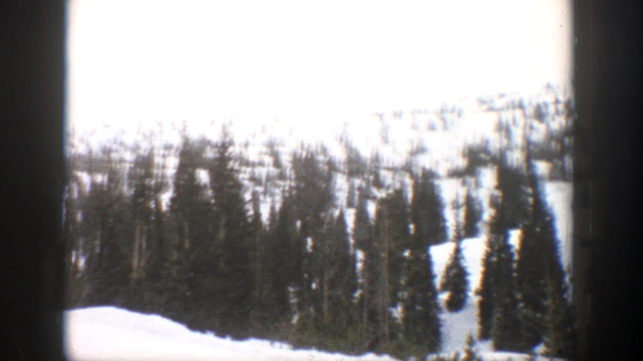 1961 Aspen, Colorado 8mm frame showing snow-covered evergreens on a mountain slope under a cloudy sky.