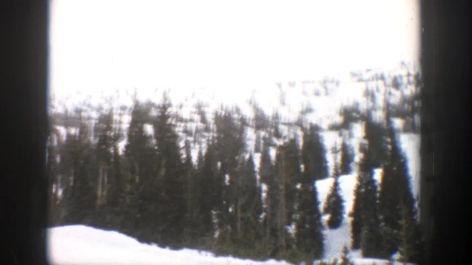 1961 Aspen, Colorado 8mm frame showing snow-covered evergreens on a mountain slope under a cloudy sky.
