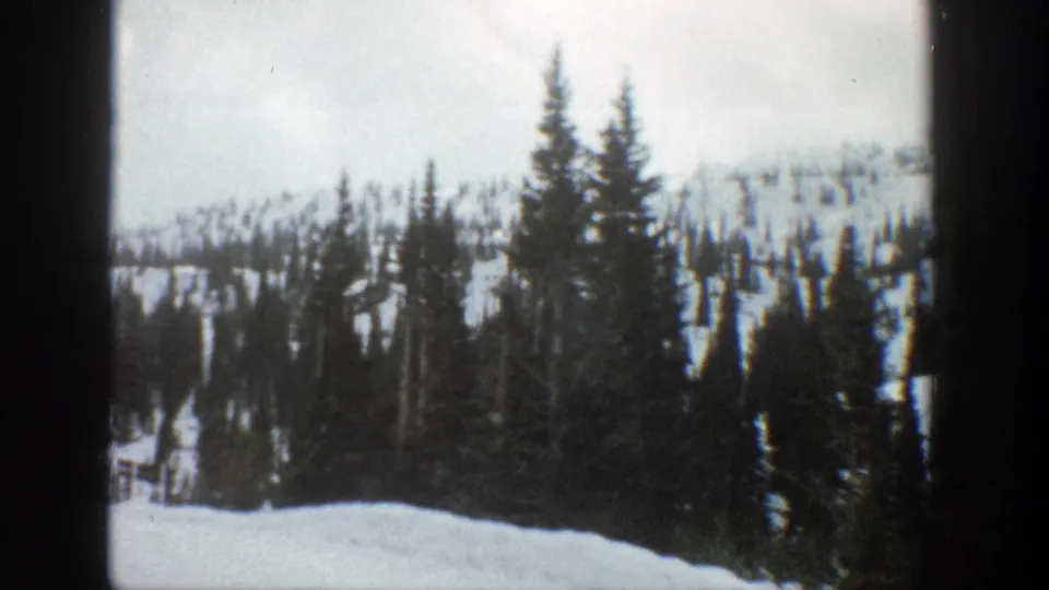 Snow-covered Aspen mountain landscape with tall evergreens and dark window-like borders in a 1961 8mm home-movie frame.