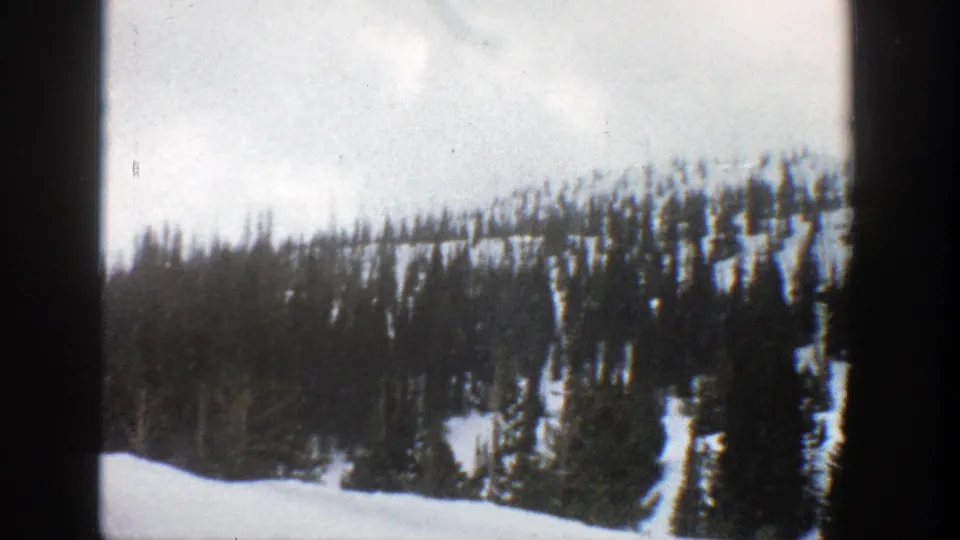 1961 Aspen-area 8mm frame showing a snow-covered evergreen slope and dark vertical film borders.