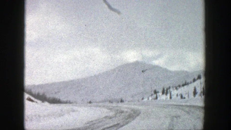 A snow-packed road curves through an Aspen, Colorado mountain landscape in this 1961 8mm frame.