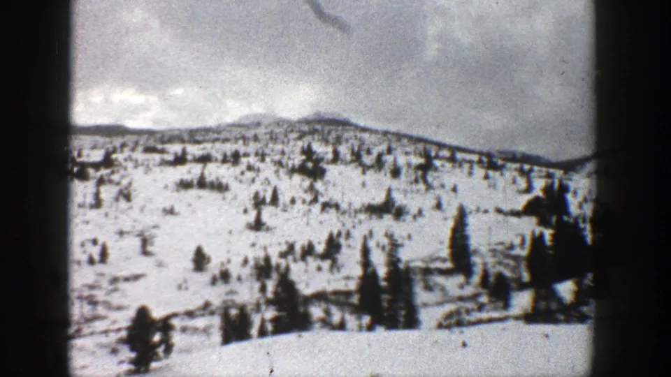 1961 Aspen, Colorado home-movie view of a snowy evergreen-dotted hillside with a low mountain ridge and dark film-edge framing.
