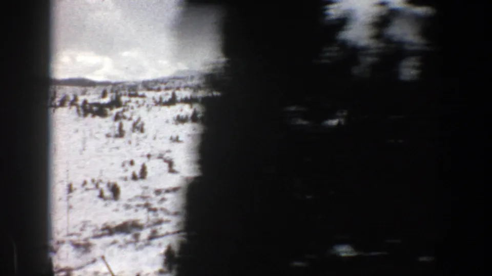 1961 Aspen-area winter landscape with snow, evergreens, distant ridgeline, and dark passing foreground blur.