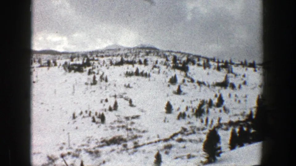 1961 Aspen, Colorado frame of a broad snow-covered hillside with sparse evergreen trees and visible film grain.