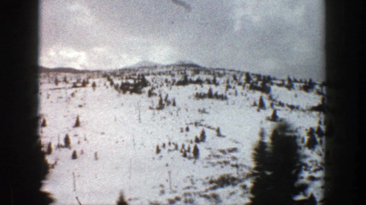 Snowy mountain hillside beside a winter road, with evergreens and dark film-frame edges.