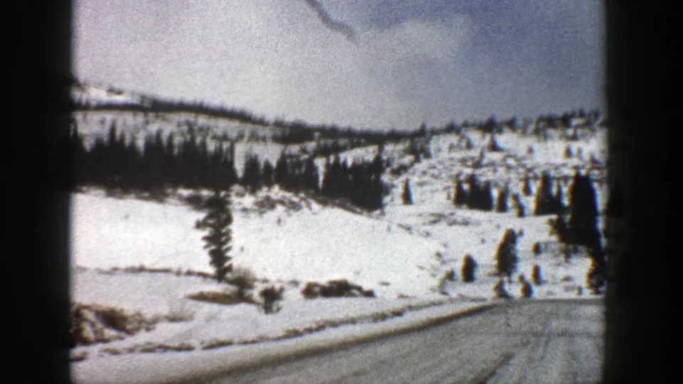 1961 Aspen, Colorado 8mm frame showing a winter road curving past snow-covered slopes and sparse evergreens.